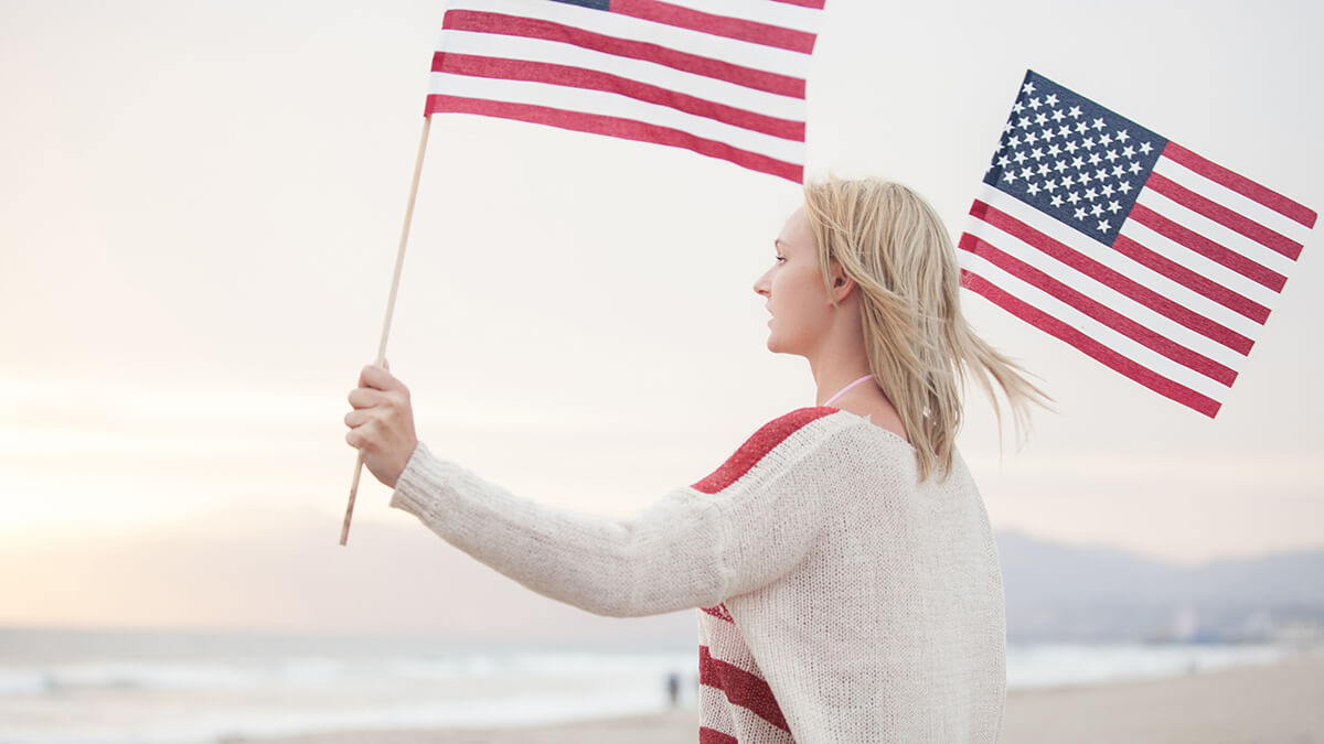 A woman in a red and white sweater holding an american flag in each hand