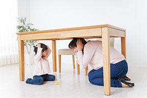 A mother and child under a sturdy table covering their heads with their hands.