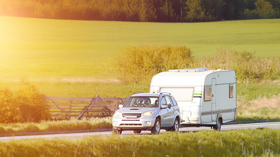 A car tows a camper trailer down a sunny road