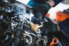 Man with gloved hand putting new oil filter in proper location