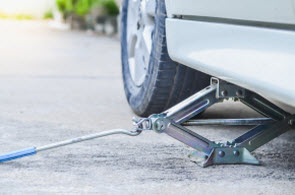 Car jack slight extended underneath car behind front wheel