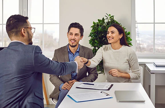 A couple smiles and shakes hands with an insurance agent.