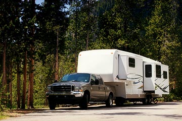 A pickup truck pulling a fifth-wheel through the scenic wilderness.
