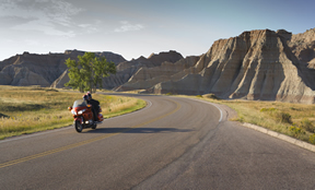 Motorcycle riding down the road with a tree and beautiful buttes in the background