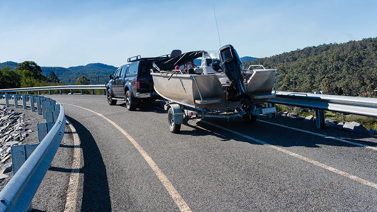 Boat on trailer being towed by pickup truck traveling on the road behind a semi