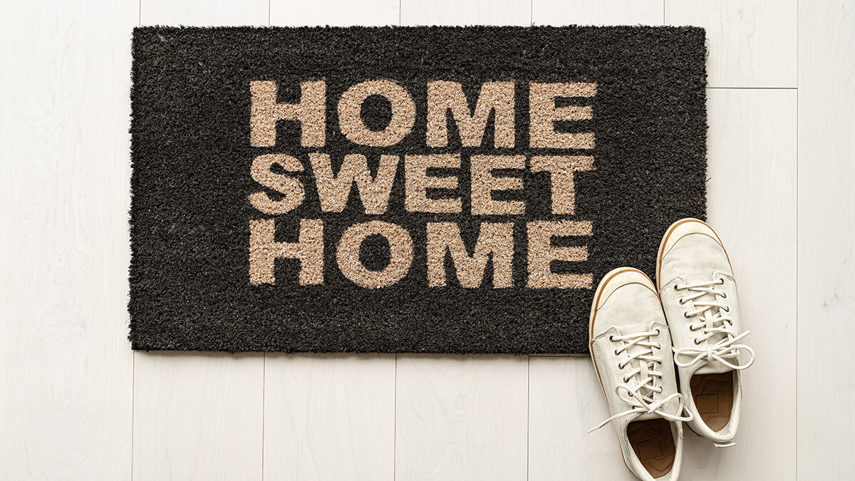 A Home Sweet Home door mat with a white pait of tennis shoes sitting on it