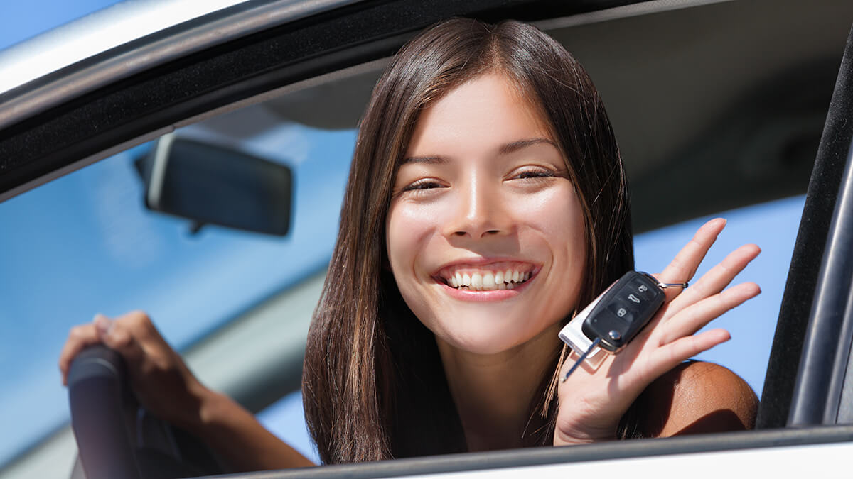 Dad handing car key to teen girl sitting in the driver seat of car