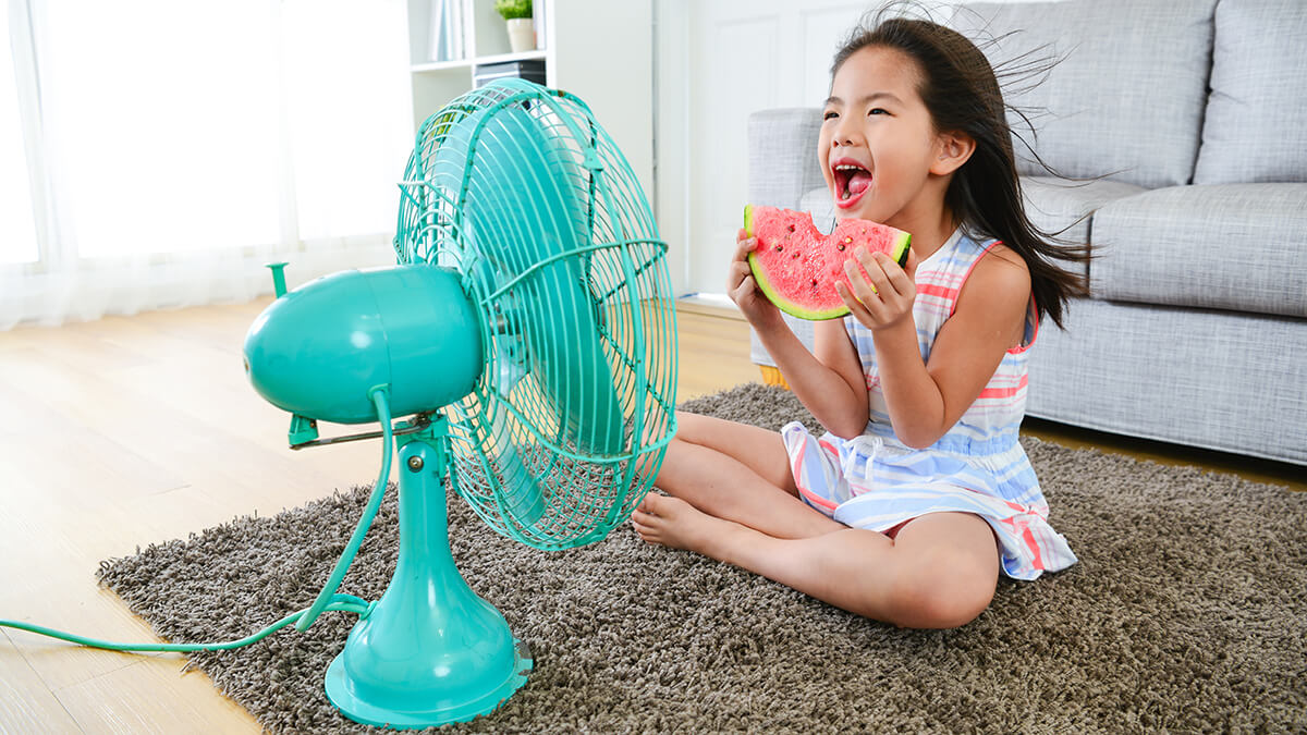 Little girl eating watermelon in front of teal colored fan