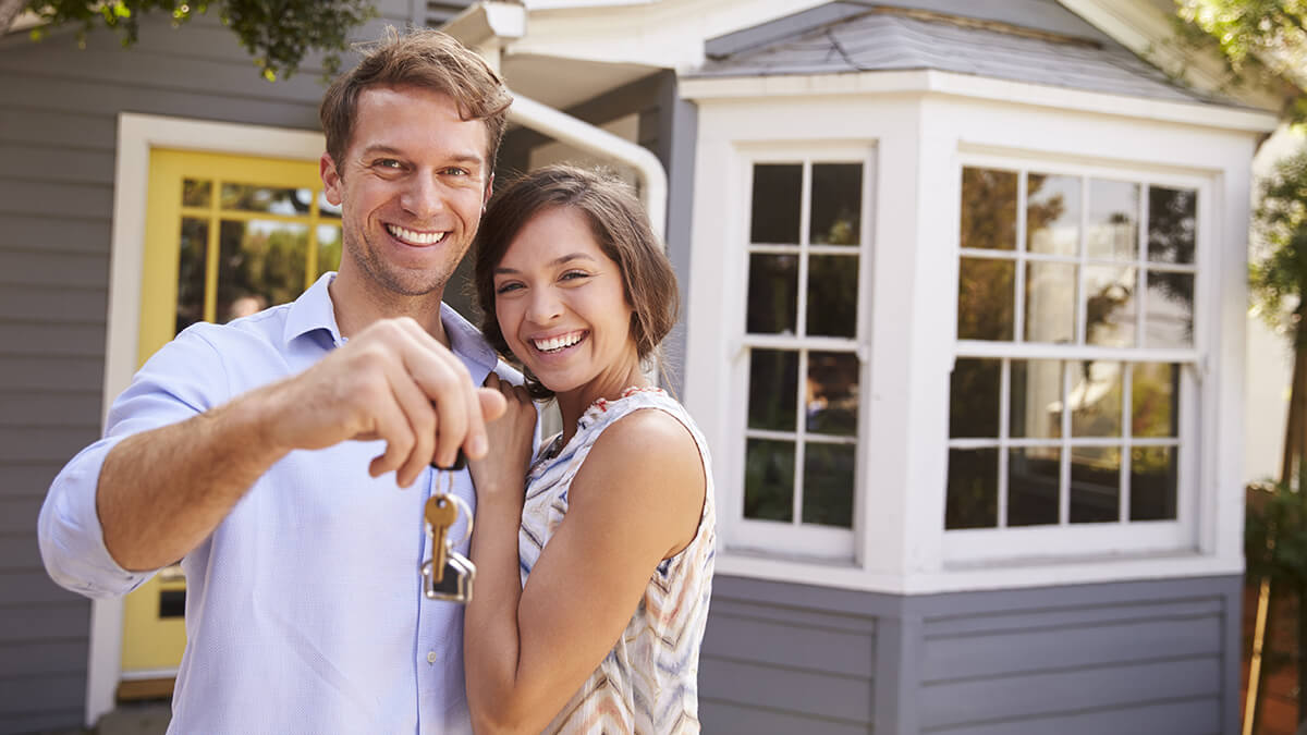 A young couple standing outside a home, the man holding keys