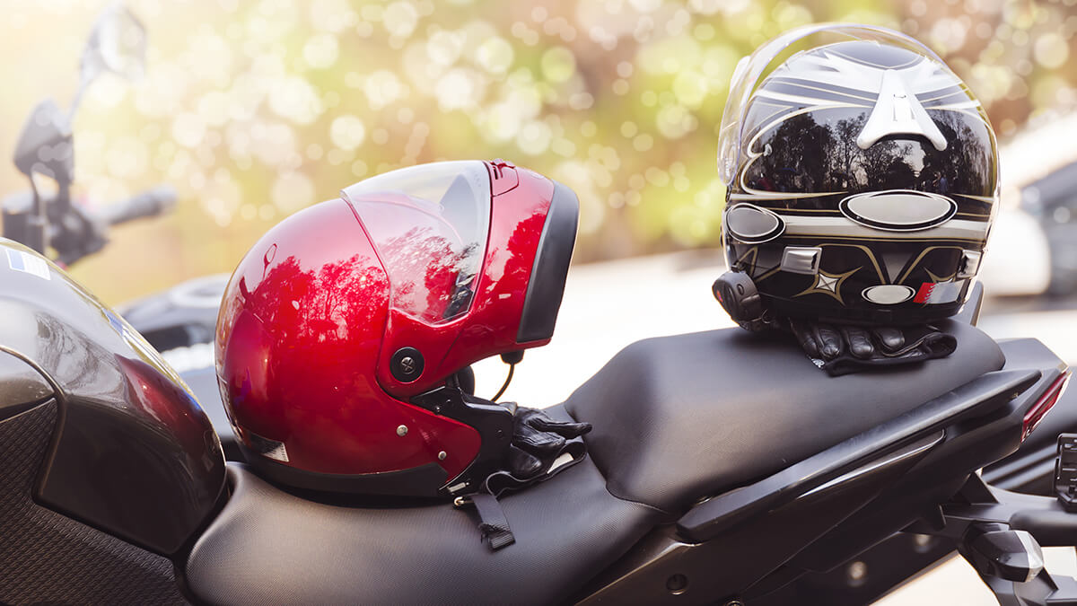 Two helmets, one red and one black, sitting on motorcycle seat