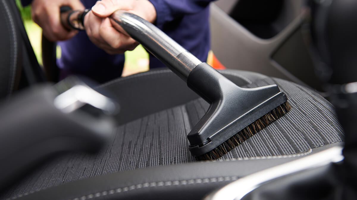 A person cleaning car seat with vaccuum