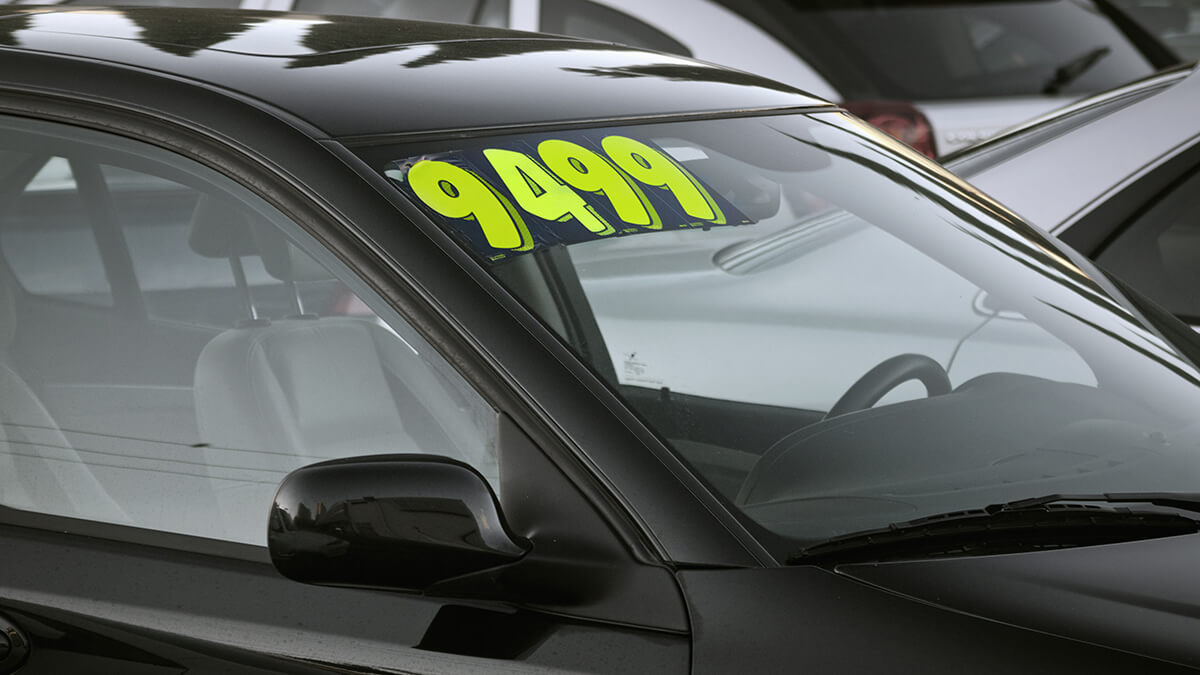 A person handing keys over to new car owner in front of car