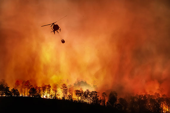 The silhouette of a helicopter flies through smoke from a wildfire.