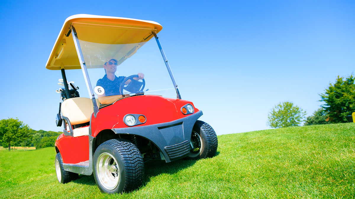 Red golf cart on a grassy, hilly fairway with only the driver and his club.