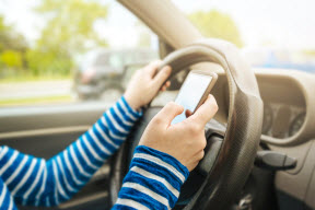Teen driving holding steering wheel and texting on cell phone