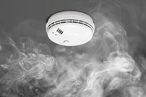 A smoke detector on the ceiling with white smoke rising towards it