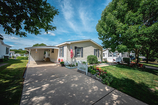 An American flag waves outside of a classic panel manufactured home in a verdant suburb.