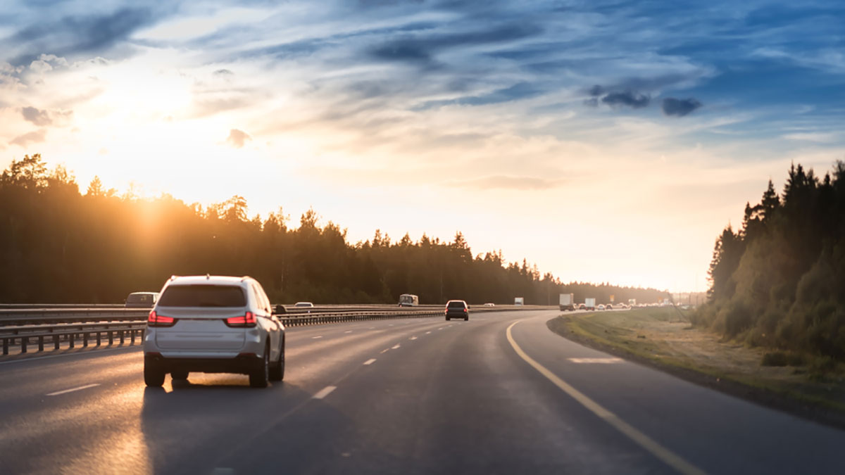 Cars driving on a tree-lined interstate as sunset.