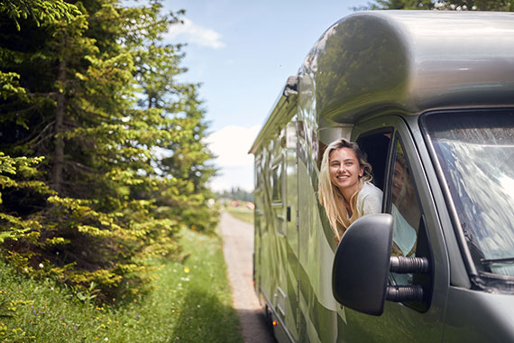 A woman leans out of the passenger side window of an RV.