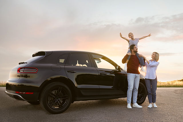 A family stands beside their car smiling in the sunset.