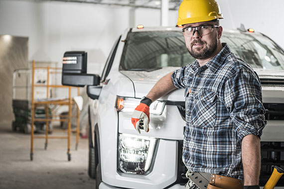 A contractor in a hard hat leans against his commercial vehicle.