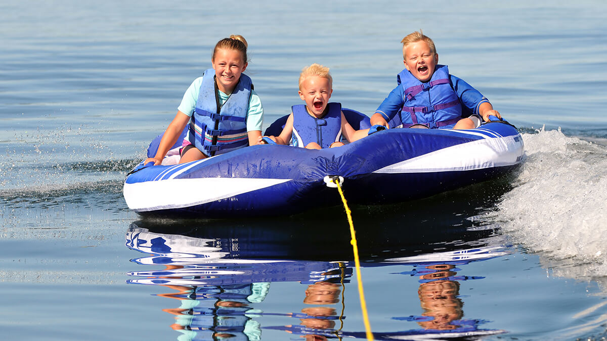 Three kids on large orange water tube smiling and having fun