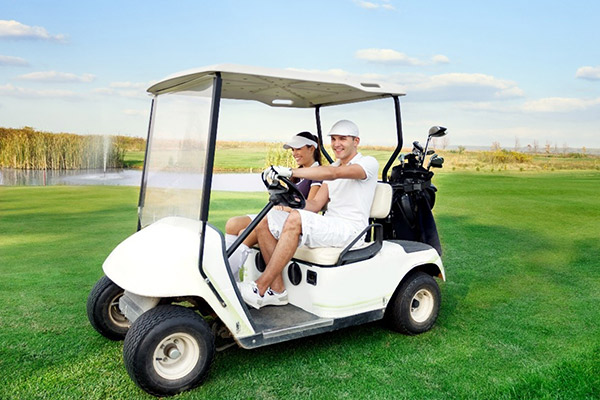 A young couple in a golf cart driving on a golf course