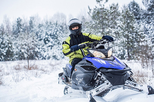 A snowmobiler driving on a trail near the edge of the woods