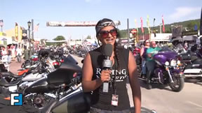 A reporter with microphone in front of rows of motorcycles
